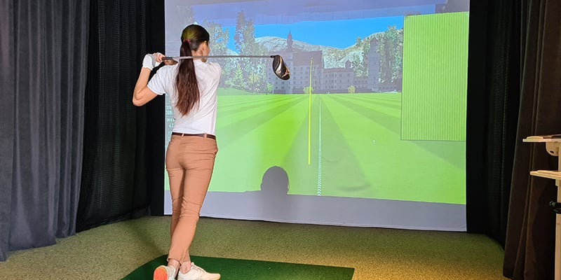 Female golfer plays golf on golf simulator.